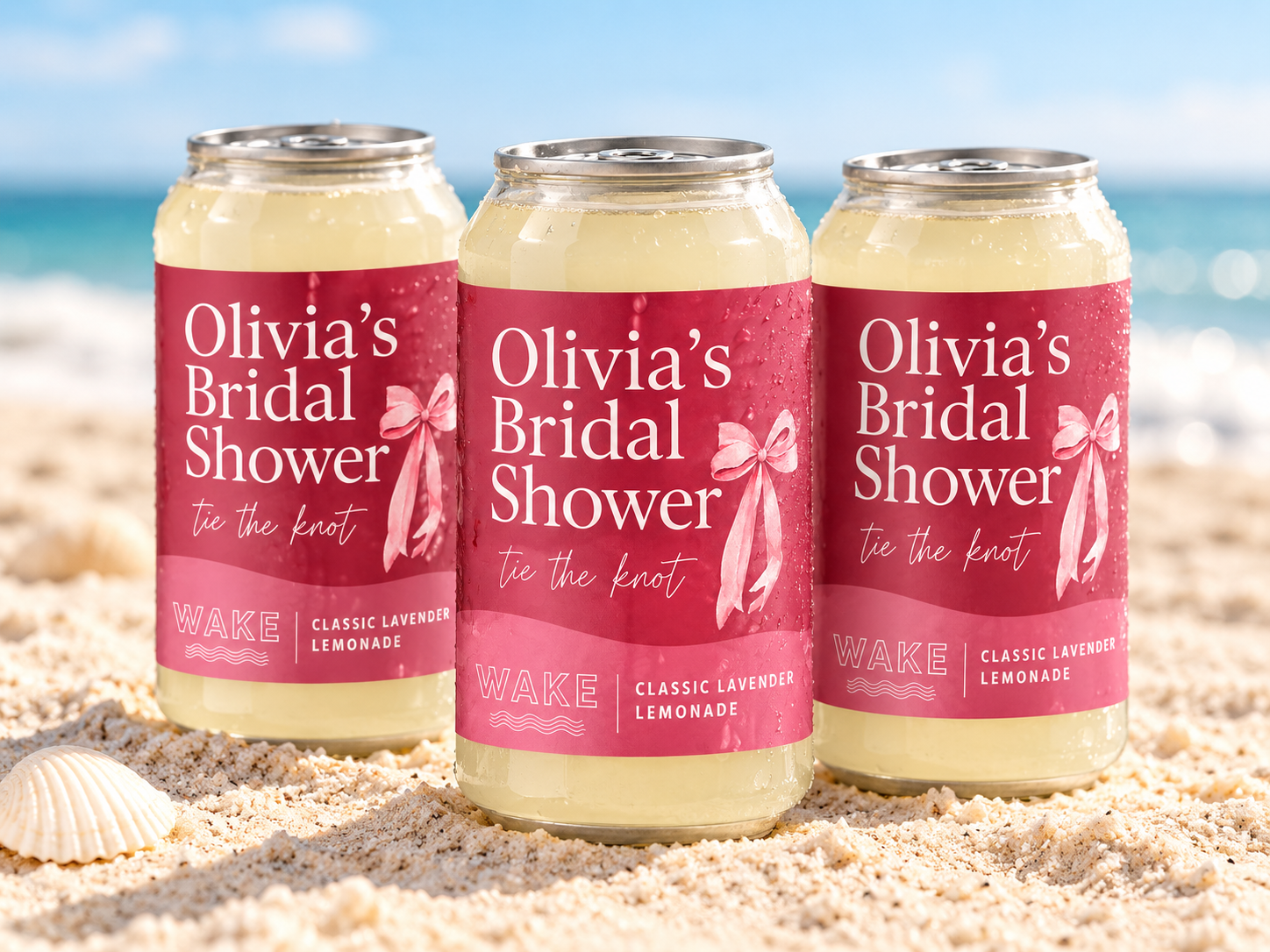 Three custom Olivia's Bridal Shower WAKE Classic Lavender Lemonade cans standing in the sand at the beach