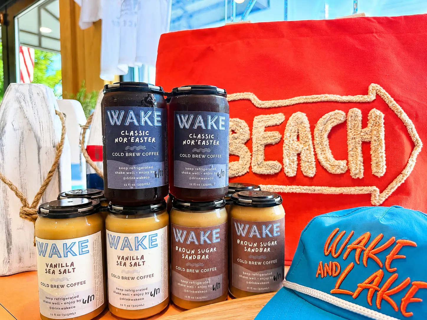 WAKE cold brew cans displayed with a beach sign and WAKE and Lake hat at a local retailer